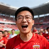 一位戴眼镜的中国男性球迷头像照片，穿着红色球迷T恤，背景是模糊的球场看台，表情兴奋。